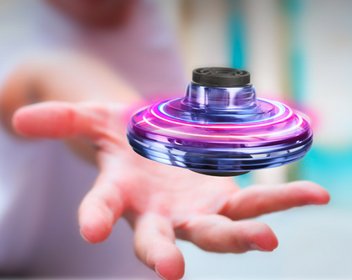 A close-up shot of a person holding a spinning, glowing, circular gadget mid-air. The device, known as the Mini Drone LED UFO Type Flying Helicopter Spinner Fingertip by Maroon Asteria, has a transparent outer shell with vibrant pink and white LED lights, creating a striking effect. The background is blurred to focus on the gadget’s mesmerizing RGB lights.