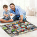 A man and child smile playing with Lacatang Shop's City Traffic Play Mat for Babies, an educational road map carpet featuring roads, buildings, toy vehicles, car parking spots, and traffic signs. They sit on a soft white rug in a bright room.