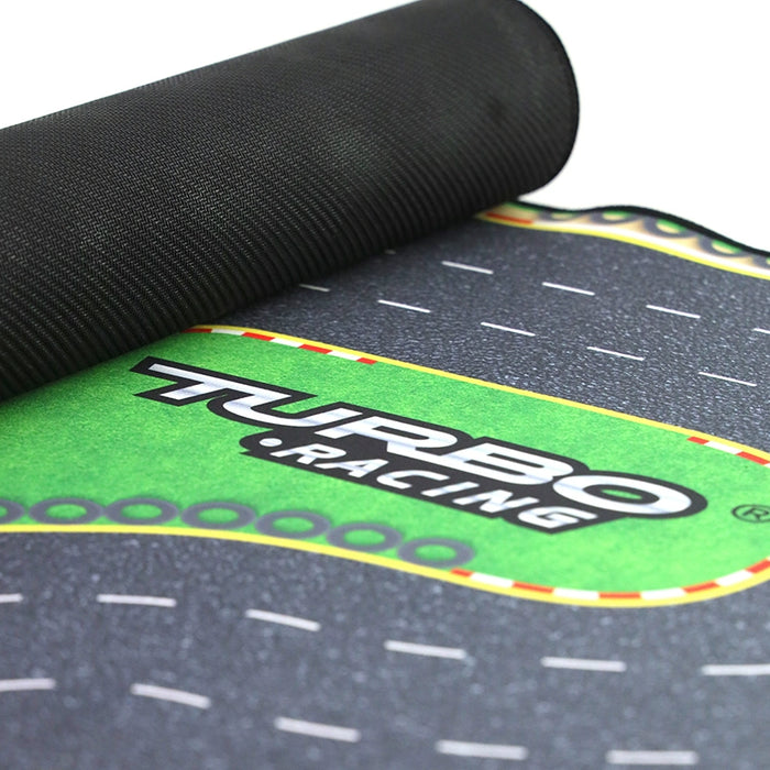 A close-up of a rolled-out play mat from Lacatang Shop displays "Turbo Racing" on a green road design, resembling a race track. The black textured edges create the perfect setting for your Turbo Drift Remote Control Car Track for Big and Small Scenes adventure.