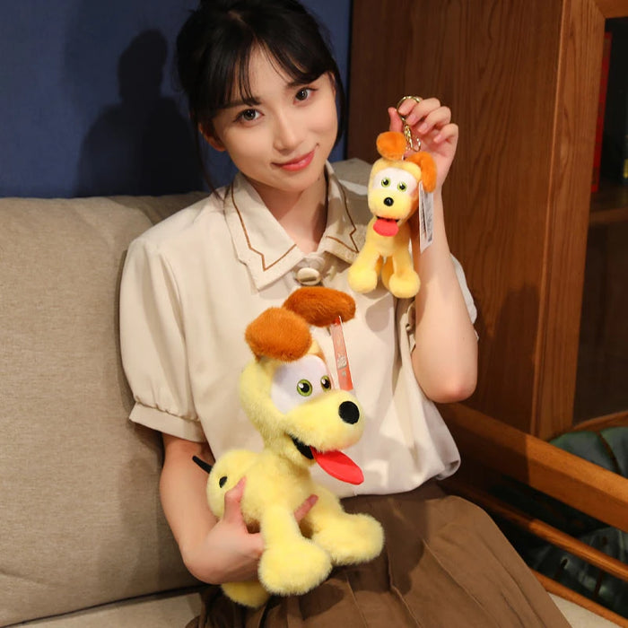 A person on a sofa smiles while holding two Kawaii Oudi Dog Plushies from Lacatang Shop, each featuring a small yellow cartoon-style dog with brown ears and a big red tongue. Perfect for anime lovers, they wear a beige blouse and brown skirt. Ideal for room decor or as an Xmas gift!.