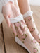 A person adjusts Lacatang Shop's Delicate Vintage Floral Lace Ruffle Socks with Crystal Silk, featuring a pink rose pattern and green leaves. These kawaii Harajuku style crew socks have a soft white cuff and grace a wooden floor.