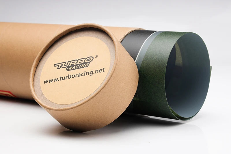 A cardboard tube with one end open shows blue and green sheets ideal for a customizable track. The lid beside it displays the "Turbo Racing" logo and website. Perfect for remote control car fans, the TURBO RACING Track Mat from Lacatang Shop offers an adaptable racing surface with cement blocks and drift jumps.