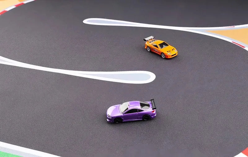 On the Lacatang Shop Large 160x90cm Portable Turbo Racing Rubber Track Mat, a sleek black surface with white and red borders, two 1:76 RC mini cars—a purple car leading an orange one—navigate sharp curves in dynamic motion.