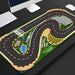 The Lacatang Shop Portable Turbo Racing Rubber Track Mat for 1:76 RC Cars, featuring winding roads, a checkered start/finish line, parking lot, and pond design is on a black desk with enhanced grip alongside a white keyboard. Available in 160x90cm & 180x80cm sizes.