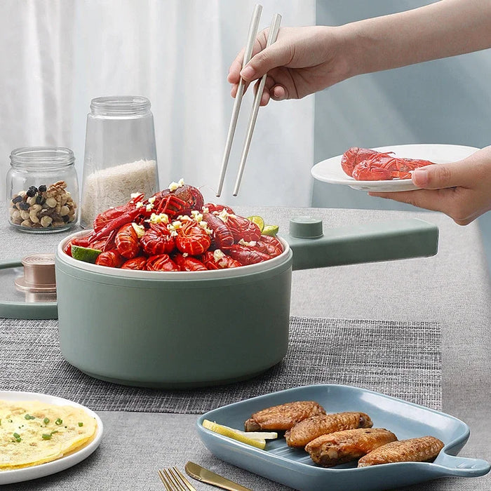 A person uses chopsticks to pick up a piece of cooked seafood from a bowl filled with a seafood dish, prepared with the 2024 New Portable 1.5L Multi-function Pot Rice Cooker Electric Cooking Stir Frying Noodle Pot Mini Hot Pot Household Dormitory from Lacatang Shop. The table also has plates with chicken wings, a folded omelet, and jars containing spices and grains. Everything is set on a gray placemat.