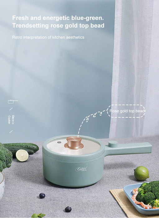 A 2024 New Portable 1.5L Multi-function Pot Rice Cooker Electric Cooking Stir Frying Noodle Pot Mini Hot Pot Household Dormitory from Lacatang Shop, featuring a stylish blue-green design with a rose gold top bead handle, sits on a kitchen counter. Surrounding it are an assortment of vegetables, including broccoli, cucumber, and a bowl of salad. In the background, a gray curtain is partially visible with descriptive text overlayed on the image.