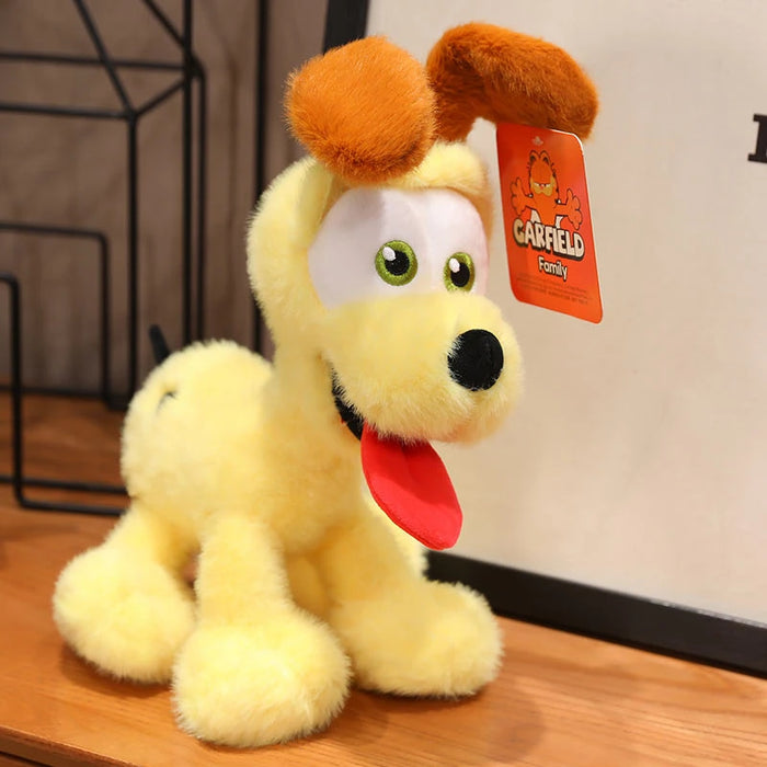 A yellow kawaii Oudi Dog Plushie from Lacatang Shop features brown ears, a red tongue, large expressive eyes, and a "Garfield Family" tag. Ideal as a cute and quirky design for anime enthusiasts.