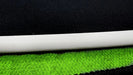 A close-up of a white cylindrical object sits on layered green and black fabric, similar to the Lacatang Shop TURBO RACING 1:76 Remote Control Car Race Track Set. The green fabric has a small circular pattern, while the black fabric showcases a larger rough texture.