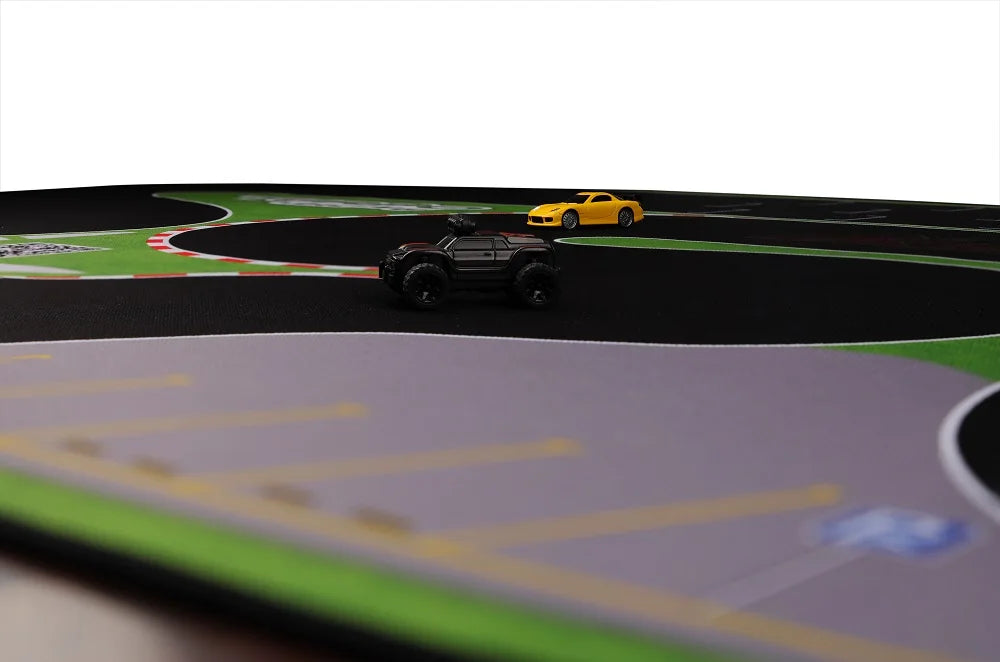 Mini RC cars race across the Lacatang Shop's Turbo Racing Rubber Mat, with a black car leading and a yellow one chasing on this portable track, featuring winding roads and parking spaces.