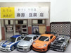 A display featuring four 1/43 scale 2.4G RC Drift Cars in front of a miniature Japanese tofu shop. The cars from Lacatang Shop include a blue and white sports car, a silver car, an orange car, and a black and white camouflaged car. The shop sign above reads "Handmade Tofu Shop" in Japanese.