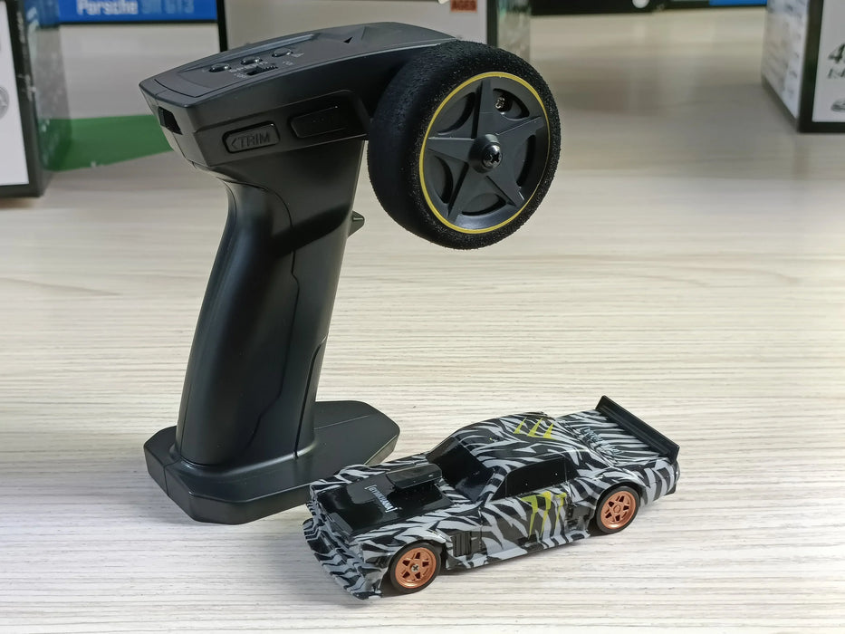 A black and gray remote control device with a large wheel is placed on a light wood surface. Beside it sits the 2.4G RC Drift Car 1/43 4WD High Speed Four Wheel Drive Radio Controlled Mini Racing Car Model by Lacatang Shop, showcasing a striking zebra-striped pattern, black roof, and vibrant orange wheels. The background includes blurred images of product boxes, hinting at thrilling high-speed racing car accessories.