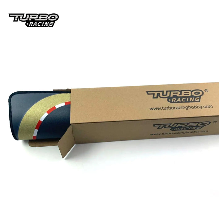 An open brown cardboard Lacatang Shop box shows a TURBO RACING 1:76 Scale RC Car Track Kit, featuring a rolled-up racing mat with white, red, and gold lines for customizable layouts, perfect for remote control car adventures with drift jump and cement blocks.