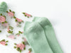 Close-up of Delicate Vintage Floral Lace Ruffle Socks from Lacatang Shop, featuring pink floral embroidery with green leaves and solid mint green foot and toe sections. These crystal silk crew socks embody a kawaii Harajuku style, elegantly displayed on a white background.