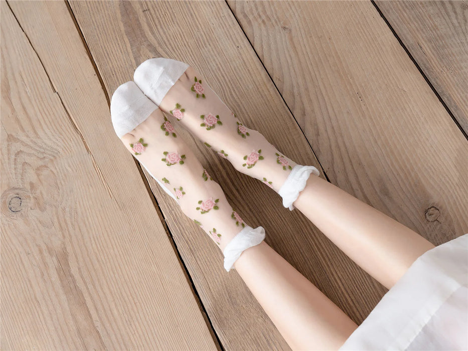 Resting on a wooden floor, this person wears Lacatang Shop's Vintage Floral Lace Ruffle Socks featuring pink rose designs, white toes, and ruffled cuffs, combining the kawaii Harajuku style with elegant ultra-thin transparent crystal silk.