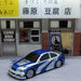 A detailed 2.4G RC Drift Car 1/43 from Lacatang Shop, featuring a high-speed four-wheel drive and a striking blue and silver paint job, is parked in front of a small storefront adorned with Japanese signage. The store boasts a brick lower facade, large windows, curtains, and traditional noren hanging above the entrances.