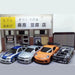 Four detailed models of the 2.4G RC Drift Car 1/43 from Lacatang Shop are displayed in front of a miniature building facade. The cars come in blue, silver, orange, and black with white patterns. A yellow sign above the building entrance has Japanese text, creating an urban storefront backdrop.