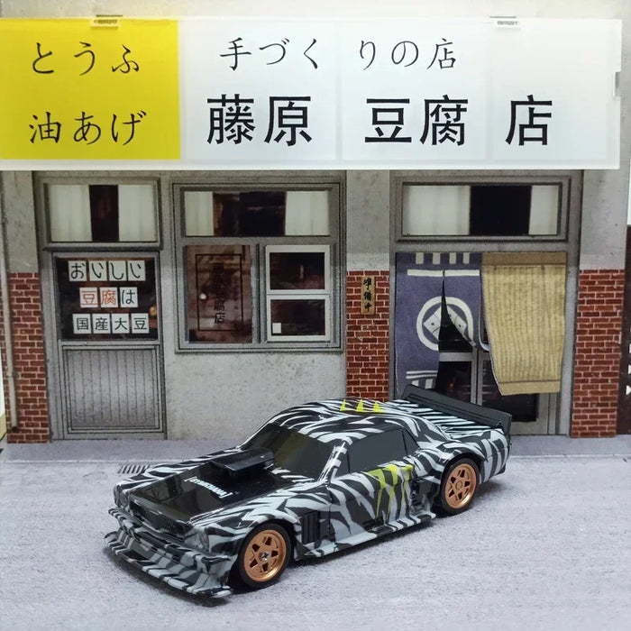 A 2.4G RC Drift Car 1/43 4WD Remote Control Car High Speed Four Wheel Drive Radio Controlled Mini Racing Car Model from Lacatang Shop, featuring a black and white camouflage pattern with gold wheels, is placed in front of a small Japanese shop with a sign reading "藤原 豆腐 店" and an awning. The shop has large windows and a door with a curtain, creating the perfect backdrop for this detailed collectible.