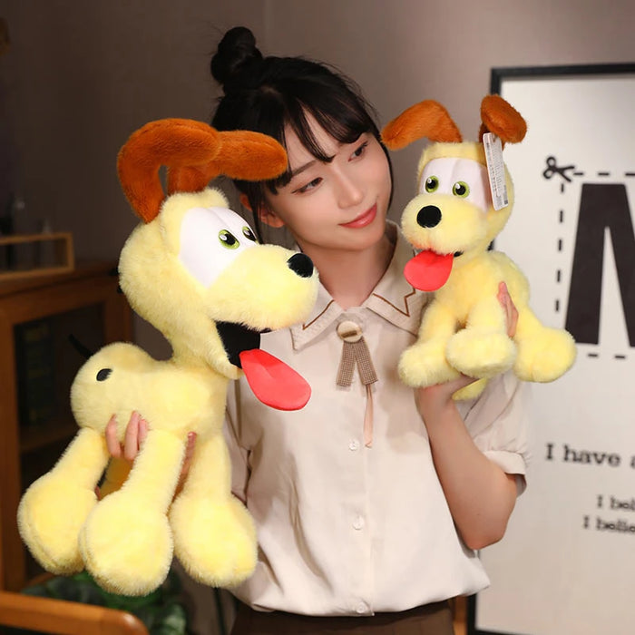 A dark-haired person in a bun holds two Lacatang Shop's Kawaii Oudi Dog Plushies. These plushies, resembling cute cartoonish yellow dogs with big eyes, floppy brown ears, and large red tongues, perfectly complement their warm smile and beige blouse—a delightful scene for anime lovers.