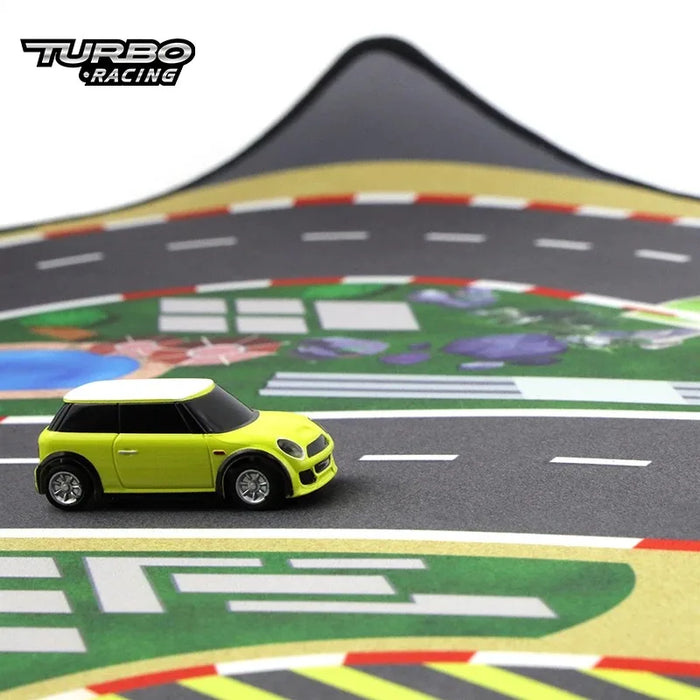 A tiny lime green toy car races on Lacatang Shop's Portable Turbo Racing Rubber Mat, a vibrant racetrack-themed play mat featuring curves and the "Turbo Racing" logo in the top left corner, perfect for 1:76 RC mini cars.