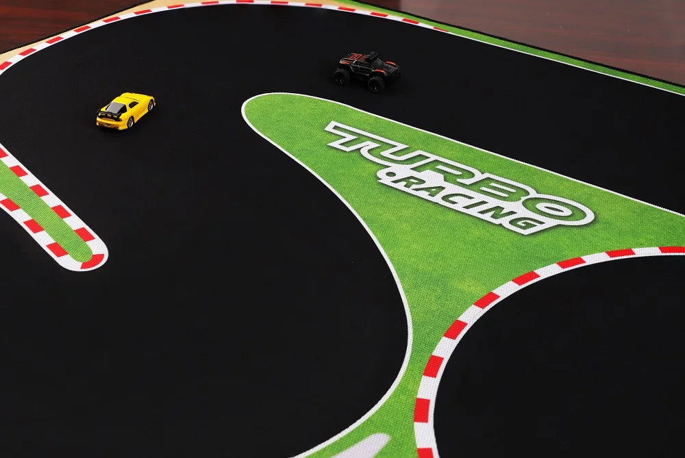 The Lacatang Shop Turbo Racing Portable 1600x900mm Table Race Track Mat features a black surface with red-and-white borders. A small yellow car and a black truck race on the mat, while a green section displaying "Turbo Racing" is visible on the right. Suitable for scales 1/76, 1/64, and 1/58 mini RC cars.