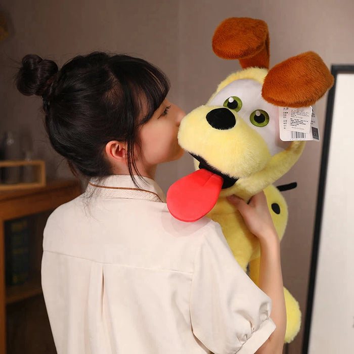 A dark-haired person gently kisses a Lacatang Shop Kawaii Oudi Dog plush toy, capturing its charm. This yellow toy, with brown ears, big eyes, and a playful red tongue, adds warmth to the room décor as seen against a soft-focus backdrop.