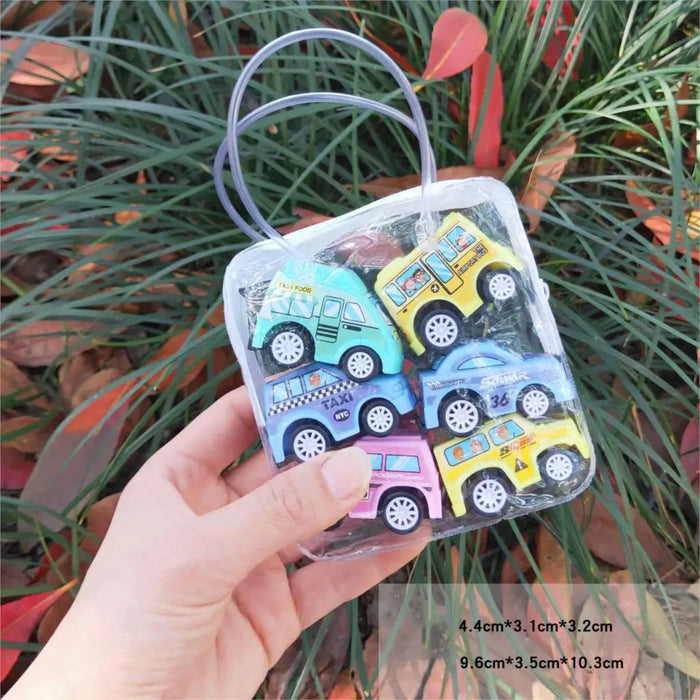 A hand holds a transparent bag with six colorful toy cars in blue, yellow, pink, and green shades atop the City Traffic Play Mat for Babies by Lacatang Shop. The lush grass and red leaves create a vibrant backdrop, displaying the educational road map carpet's theme of road safety.