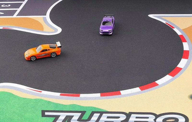 Two 1:76 RC Mini Cars, one orange with a spoiler and one purple, are on the Large Portable Turbo Racing Rubber Mat from Lacatang Shop. This racetrack-themed mat has curved red and white borders with "TURBO" emblazoned on its surface.