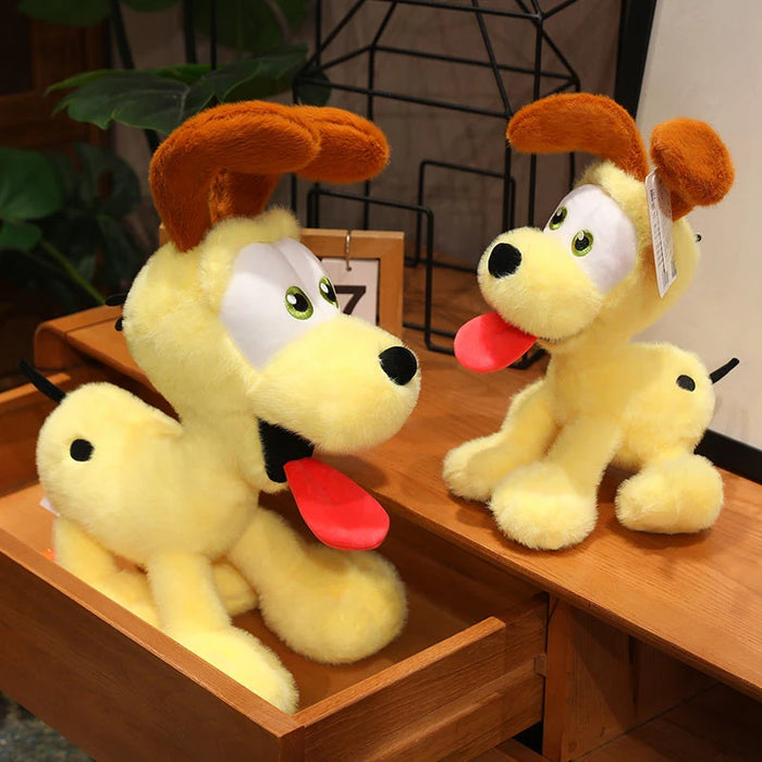 Two Lacatang Shop Kawaii Oudi Dog plush toys, featuring yellow fur, brown ears, red tongues, cheerful expressions, and black spots, sit in and on a wooden drawer. The background includes part of a plant and a decorative metal structure.