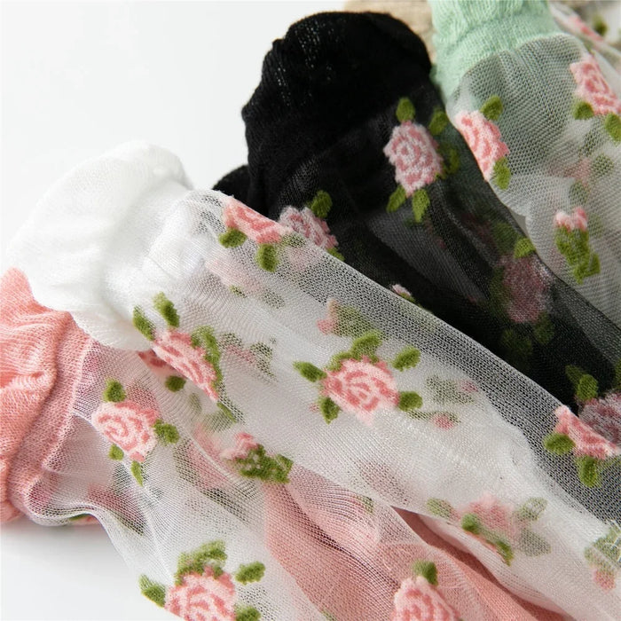 A close-up of Lacatang Shop's Delicate Vintage Floral Lace Ruffle Socks with Crystal Silk, featuring intricate embroidery and kawaii Harajuku style, available in white, black, pink, and green. Each pair showcases charming pink and green floral patterns.