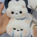 A person holding two fluffy white Cartoon Plush Rabbit Doll Toy Keychains from Lacatang Shop, each resembling cute, round-faced rabbits. Made from high-quality plush material, one keychain features a neutral expression with blush on its cheeks, while the other displays a sad expression with blue tear marks under its eyes. The durable zinc alloy clips ensure long-lasting use.