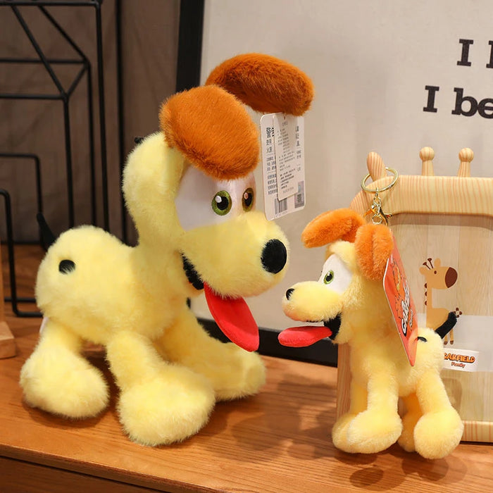 A large and a small Kawaii Oudi Dog plushie by Lacatang Shop sit on a wooden shelf. Both have yellow fur, brown ears, big eyes, and red tongues. The larger has a visible tag; the smaller is attached to a frame. Perfect for anime lovers who enjoy cute and quirky designs.