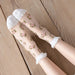 Feet rest on wooden floorboards adorned in Lacatang Shop's Delicate Vintage Floral Lace Ruffle Socks, a kawaii Harajuku style with pink rose patterns and white ruffled cuffs.