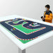 A child in a yellow jacket and mask holds a remote by the Lacatang Shop's LDARC Mini RC Car Racing Track Mat on a table, featuring 1/76, 1/64, and 1/58 scale vehicles with mini buildings on a black surface with red-and-white barriers.