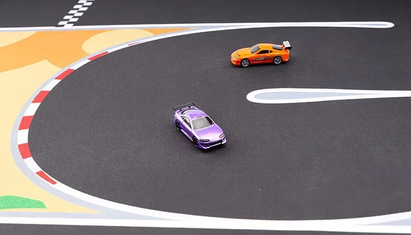 Two RC mini cars, one purple and one orange, race on Lacatang Shop's Portable 1/76 Scale Turbo Racing Rubber Mat. The black track features white, red, and orange designs for a realistic racing experience.