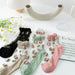 A white table displays five pairs of Lacatang Shop's delicate vintage floral lace ruffle socks with crystal silk in black, beige, green, pink, and white. Daisies, an abstract vase, a glass of water, and a green "EN Spain" magazine complete the Kawaii Harajuku style scene.