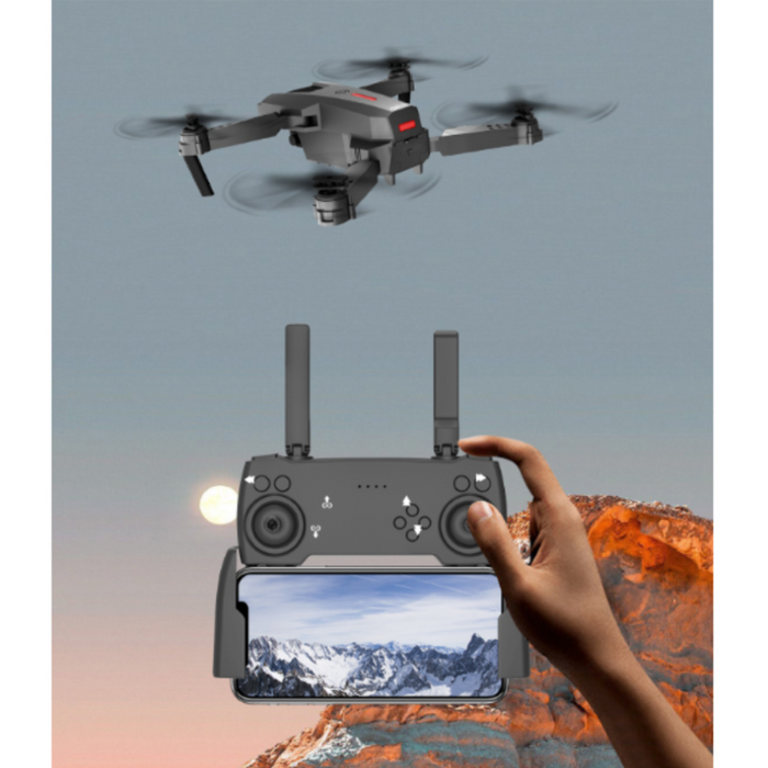 A person operates a Yellow Pandora Ninja Dragon Phantom X HD Dual Camera Smart Quadcopter Drone using a remote controller with a smartphone attached, displaying a mountain landscape. The smart quadcopter drone is flying in a clear sky above rocky terrain, with the backdrop featuring either a setting or rising sun captured by the HD dual camera.