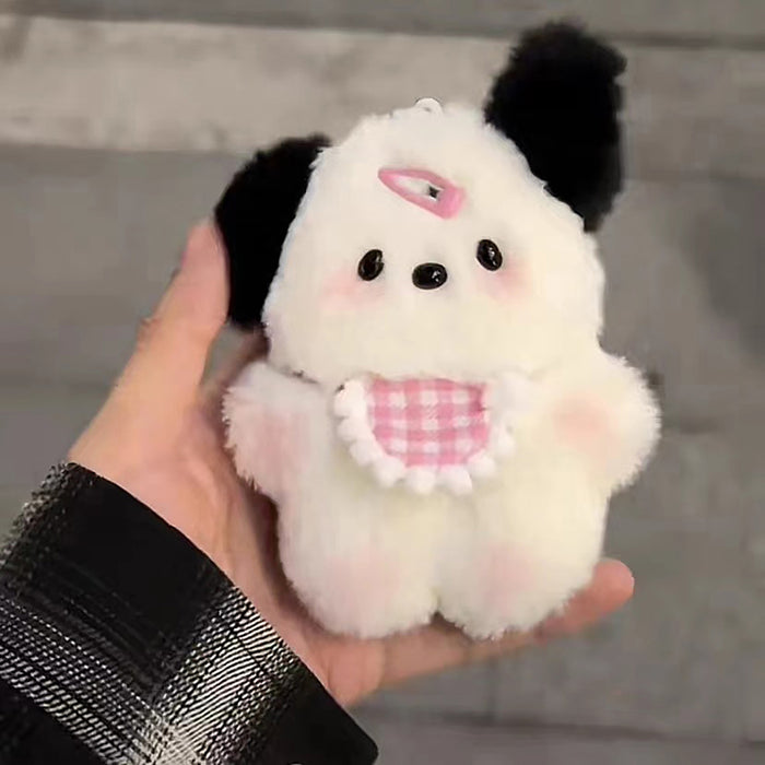 A person holding a Cute Plush Puppy Keychain by Lacatang Shop. This adorable cartoon bag charm has black-and-white fur, round eyes, pink cheeks, a checkered bib, a black ear, and a top loop—ideal as a birthday gift for women and girls. The background is blurred.