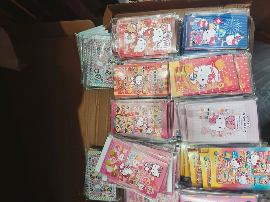 A box with kawaii phone cases featuring cute cartoon designs in pink and pastel themes, showcasing Hello Kitty characters, is neatly organized in transparent packaging sealed with Lacatang Shop's Kawaii Hello Kitty Sealing Stickers.