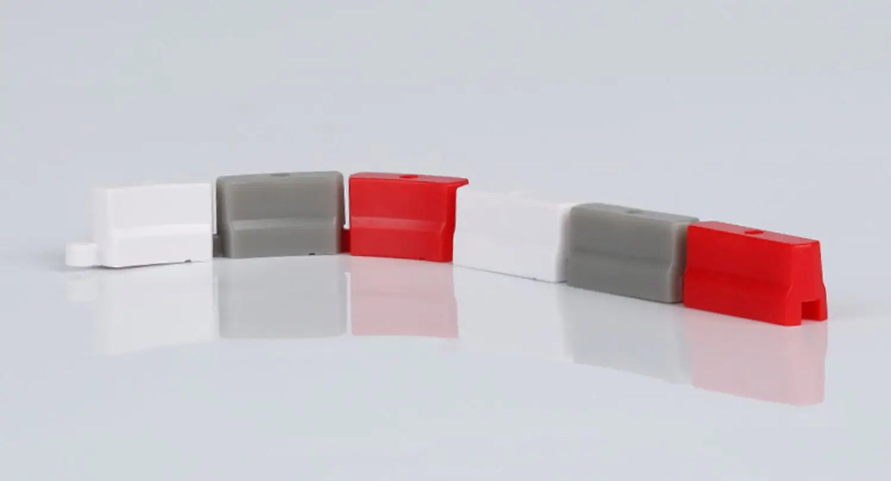 A row of small plastic traffic barriers in white, gray, and red forms an ideal setup for the TURBO RACING 1:76 Remote Control Car Racing Track Set by Lacatang Shop. Placed on a reflective surface against a plain white background, they're ready to showcase jump and drift features.