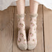 A pair of feet wearing Lacatang Shop's Delicate Vintage Floral Lace Ruffle Socks in a kawaii Harajuku style with pink roses and beige ruffled tops, featuring solid beige toes and heels. The socks exude a playful aesthetic while resting on wooden surface.