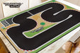 A Portable Turbo Racing Rubber Track Mat by Lacatang Shop, available in 160x90cm and 180x80cm options, features a black surface with white and red borders on a wooden table. Enhanced grip, multiple curves, and a starting line are included, with the "Turbo Racing" logo visible on the track and top left corner.