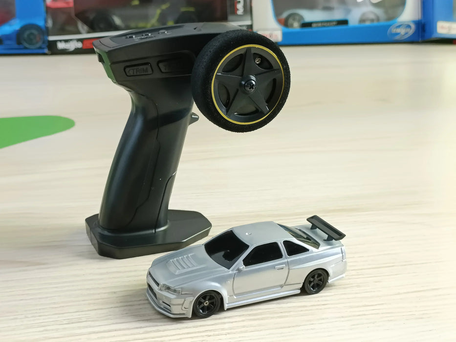 A black remote control with a steering wheel rests on a wooden surface next to the Lacatang Shop's 2.4G RC Drift Car, a silver high-speed, 1/43 scale four-wheel drive mini racing RC car equipped with a rear spoiler. Both items are located indoors, with boxed toy cars visible in the background.