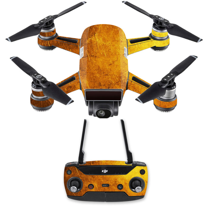 A DJI Spark Mini Drone covered in a Rose Chloe MightySkins DJSPCMB-Textured Gold Skin Decal, showcasing a golden, weathered finish, and four propellers is displayed above a remote control featuring the same design. The controller includes two joysticks, several buttons, and an antenna, all matching the drone’s vintage-like aesthetic thanks to its MightySkins protective skin.