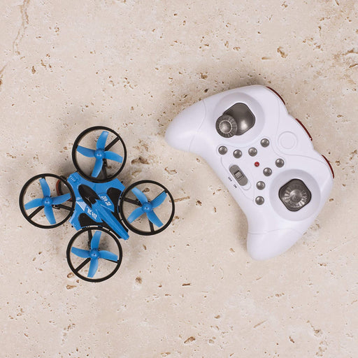 An Ivory Coeus Remote Control Mini Quadcopter, featuring a compact blue design with black propeller guards and matching blue propellers, rests on a textured beige surface. Nearby lies a white handheld controller equipped with various buttons and joysticks, promising a versatile flying experience for both novice and advanced users, further enhanced by built-in LED lights.