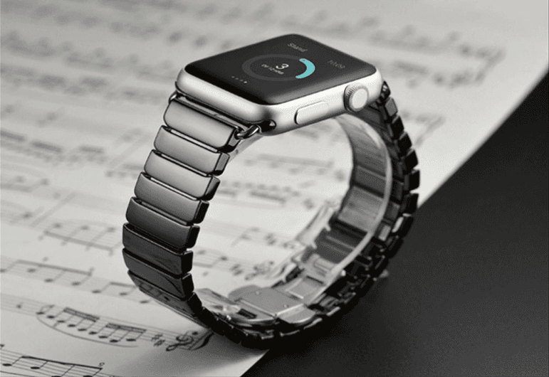 A Ceramic Apple Watch Band by Fuchsia Molly is displayed on a sheet of music. The screen reveals an activity-tracking app with circular progress indicators, set against a black and white background.